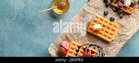 Leckere belgische Waffeln mit Beeren und Honig auf blauem Hintergrund mit Platz für Text Stockfoto