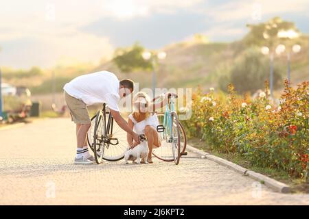 Reifes Paar mit Fahrrädern und Hund beim Spaziergang im Stadtpark am Sommertag Stockfoto
