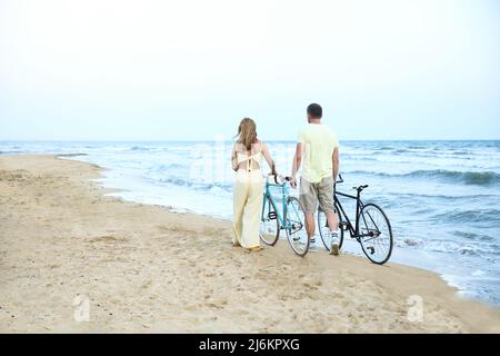 Reifes Paar mit Fahrrädern, das am Sommertag am Strand entlang läuft Stockfoto