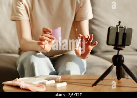 Kurzaufnahme einer jungen Frau, die Tampon und Menstruationstasse vor der Kamera vergleicht und Lehrvideo, Kopierraum, filmt Stockfoto