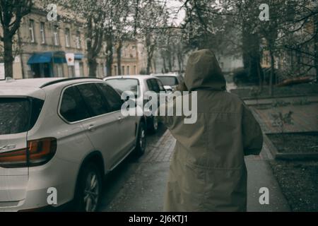 Reisende junge Frau in grünem Regenmantel mit Kapuze, die die Straße entlang läuft Stockfoto