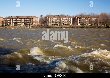 Eigentumswohnungen am Ufer des Flusses Mille-Iles mit hohem Wasserstand im Frühjahr, Terrebonne, Lanaudiete, Quebec, Kanada. Stockfoto