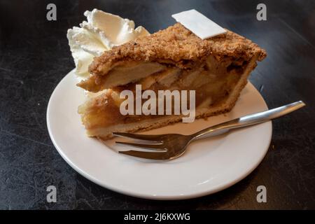 Ein Stück Apfelkuchen in Scheiben mit Schlagsahne auf schwarzem Tisch. Stockfoto