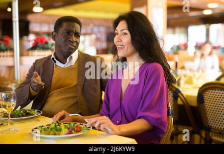 Fröhlicher afroamerikanischer Mann, der im Restaurant mit einer asiatischen Frau flirtet Stockfoto