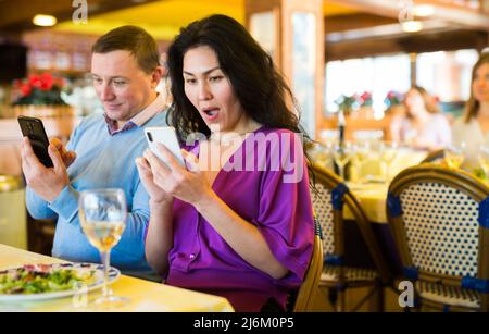 Ein erwachsenes Birazialpaar benutzt während des Mittagessens im Restaurant ein Telefon Stockfoto
