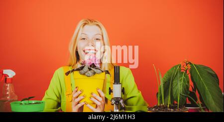 Glücklicher Blumenhändler posiert mit Blume zur Kamera. Porträt einer fröhlichen Dame im botanischen Garten. PIN up Mädchen mit blonden Haaren halten violett. Porträt von Stockfoto