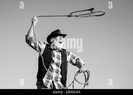 Alter Wilder Westen Cowboy mit Seil. Bärtiger westlicher Mann wirft Lasso mit brauner Jacke und Hut fangen Pferd oder Kuh. Stockfoto