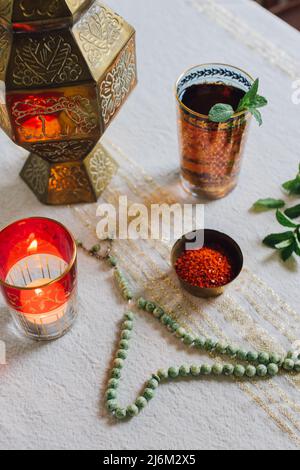 Tischgedecke mit goldenem Tuch, Aleppo-Chilischote-Flocken in Schale, Teelicht, Jadegebetsperlen, Minztee Stockfoto