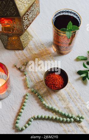 Tischgedecke mit goldenem Tuch, Aleppo-Chilischote-Flocken in Schale, Teelicht, Jadegebetsperlen, Minztee Stockfoto