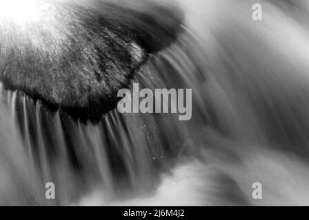 Schwarz-Weiß-Foto von Wasser, das über einen Felsen rauscht Stockfoto