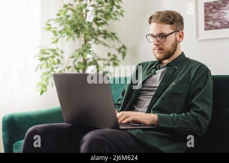 Ernsthafter Mann, der im Wohnzimmer Text auf dem Laptop tippt Stockfoto