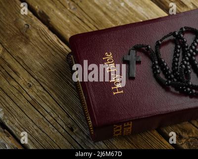 Das Buch der Heiligen Bibel mit Rosenkranz und Kreuz liegt auf einem Holztisch. Tiefes Bild.Gebet, Symbole der Spiritualität, des christentums, des katholizismus. Dort Stockfoto