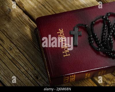 Das katholische Kruzifix liegt auf dem Buch - die Heilige Bibel auf einem Holztisch. Solarbeleuchtung. Low-Angle-Ansicht. Kirche, Gebet, Meditation, Glaube, Spiritualität Stockfoto