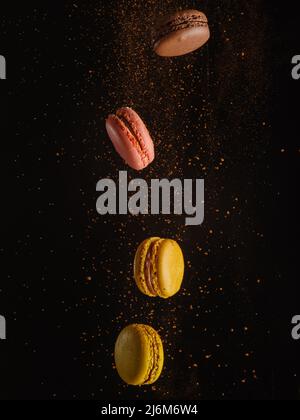 Gelbe und rosa Makronen mit einem Fluss von Schokoladensplittern in einem gefrorenen Flug auf schwarzem Hintergrund. Geburtstag, Urlaub, Süßigkeiten, Süßwaren, Geschäft. Der Stockfoto