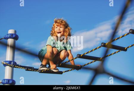 Netter Junge klettert die Leiter auf dem Spielplatz hoch. Kind klettert die Leiter gegen den blauen Himmel hinauf. Platz für Text kopieren. Stockfoto