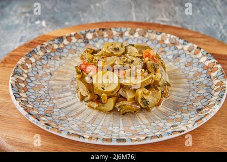 Zucchinistücke mit Tomaten auf Teller auf Holzboden Stockfoto