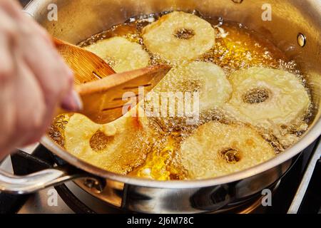 Kochen von Apfelpfannkuchen. Der Küchenchef dreht den Apfeldonut in das kochenden Öl Stockfoto