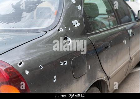 Eine Limousine mit Durchgangslöchern aus Schrapnel steht auf einem Parkplatz. Das geschälte Auto. Der Krieg in der Ukraine. Folgen des Beschuss von Zivilisten Clust Stockfoto