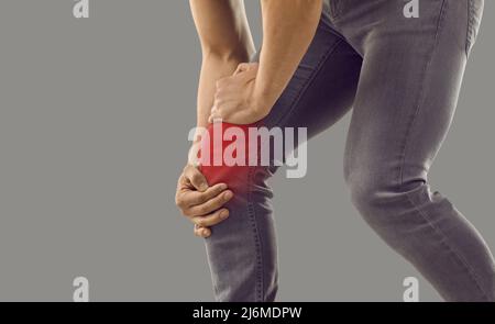 Der junge Mann, der sich am Knie verletzt hat, leidet unter Schmerzen und berührt seine Kniescheibe Stockfoto