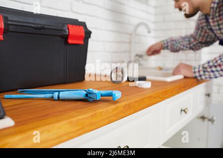 Klempner mit einem Schraubenschlüssel und anderen Werkzeugen während der Reparatur des Spülbecken Wasserhahn in der Küche Stockfoto