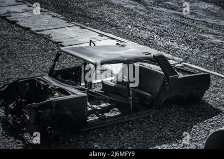 Reste von verkohltem Auto nach Explosion oder Unfall. Ansicht des Rahmens der verdrehten Maschine. Kaputte Ausrüstung. Stockfoto