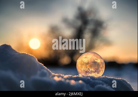 Romantische Aufnahme einer gefrorenen Seifenblase, die im Sonnenuntergang im Schnee liegt Stockfoto