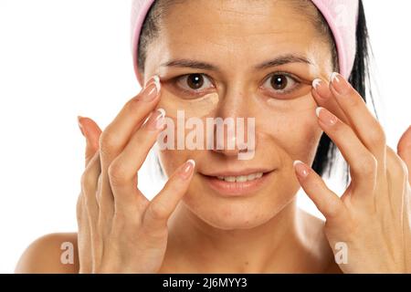 Frau mittleren Alters tragen Sie Concealer unter dem Auge auf einem weißen Hintergrund auf. Stockfoto