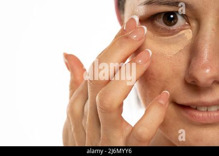 Frau mittleren Alters tragen Sie Concealer unter dem Auge auf einem weißen Hintergrund auf Stockfoto