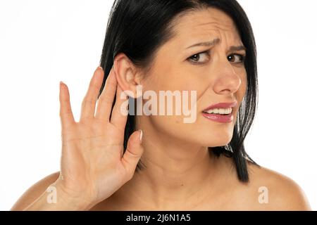 Frau mittleren Alters auf isoliertem weißem Hintergrund, die etwas hört, indem sie die Hand auf das Ohr legt Stockfoto