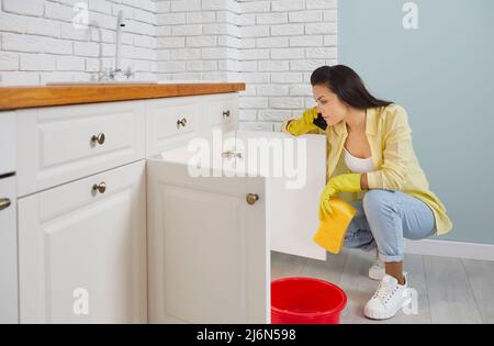 Frustrierte Frau, die telefoniert hat, Klempner wegen des undichten Rohres im Waschbecken in der Küche. Stockfoto