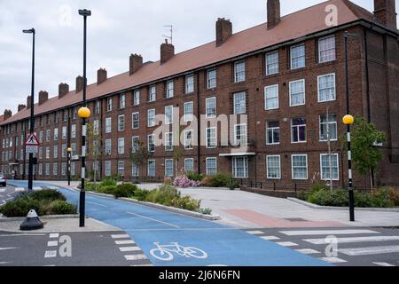 Radweg neben Sozialwohnungsblock in Shadwell am 27.. April 2022 in London, Großbritannien. Cycle Superhighway 3 oder CS3 ist ein langer Radweg und Teil des vom TfL koordinierten Radwegenetzes. Sie verläuft von Osten nach Zentral-London. Es ist eine beliebte Route sowohl für Pendler als auch für Freizeitfahrer, die entlang der Strecke eine Reihe von wichtigen Zielen in London passiert. Fast auf der gesamten Strecke werden Radfahrer auf getrennten Radwegen vom anderen Verkehr getrennt, und an größeren Kreuzungsstellen wurde die Fahrradinfrastruktur bereitgestellt. CS3 wurde jetzt in Cycleway 3 oder C3 umbenannt. Konzilsiedlungen wie Th Stockfoto