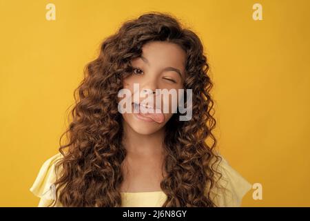 Lustiges Kind mit langen lockigen Haaren und perfekter Haut zeigt Zunge, Mode Stockfoto