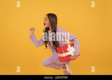 Trendy fröhlich Kind in Sonnenbrille und Anzug laufen mit Geschenk-Box zum Einkaufen Verkauf, Shopping Verkauf Stockfoto