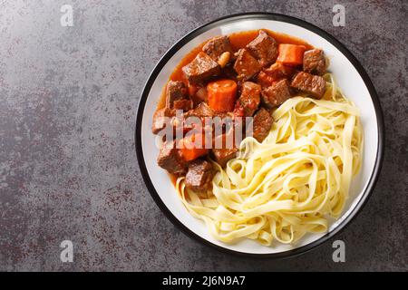 Daube de Boeuf Provencale langsam gekochter reichhaltiger Rindereintopf mit Nudeln in der Nähe auf dem Teller auf dem Tisch. Horizontale Draufsicht von oben Stockfoto