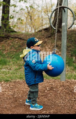 Ein kleiner Junge hält einen Boxsack in einem Park auf der Straße Stockfoto