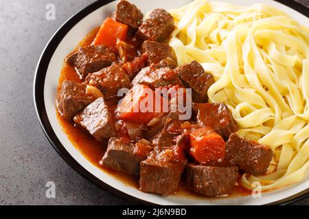 Daube de Boeuf Provencale langsam gekochter reichhaltiger Rindereintopf mit Nudeln in der Nähe auf dem Teller auf dem Tisch. Horizontal Stockfoto