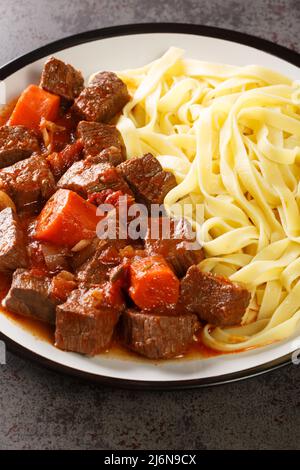 Daube provenzalisches klassisches französisches Eintopf-Rindfleisch wird langsam zu Zartheit geschmoren, serviert mit Nudeln aus der Nähe auf dem Teller auf dem Tisch. Vertikal Stockfoto