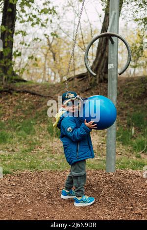 Ein kleiner Junge hält einen Boxsack in einem Park auf der Straße Stockfoto