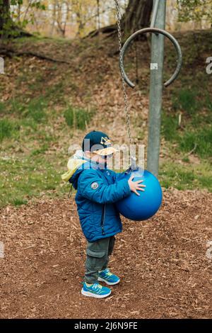 Ein kleiner Junge hält einen Boxsack in einem Park auf der Straße Stockfoto