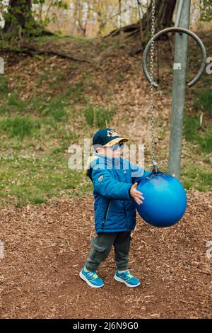 Ein kleiner Junge hält einen Boxsack in einem Park auf der Straße Stockfoto