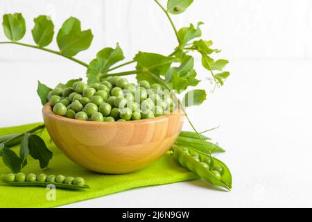 Frische grüne Erbsen in einer Holzschüssel mit Erbsen Pflanzen Blätter auf einer grünen Serviette auf weißem Hintergrund, gesundes Bohnenprotein Stockfoto