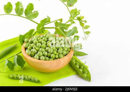 Frische grüne Erbsen in einer Holzschüssel mit Erbsen Pflanzen Blätter auf einer grünen Serviette auf weißem Hintergrund, gesundes Bohnenprotein Stockfoto