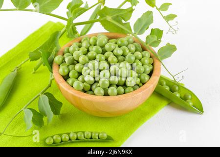 Frische grüne Erbsen in einer Holzschüssel mit Erbsen Pflanzen Blätter auf einer grünen Serviette auf weißem Hintergrund, gesundes Bohnenprotein Stockfoto