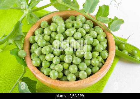 Frische grüne Erbsen in einer Holzschüssel mit Erbsen Pflanzen Blätter auf einer grünen Serviette auf weißem Hintergrund, gesundes Bohnenprotein Stockfoto