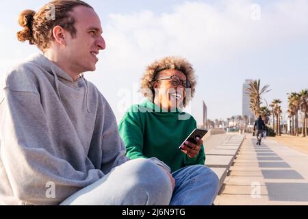 Junge lateinerin lachend auf einer Bank sitzend, Spaß mit ihrer Freundin, Konzept von Lifestyle und Freundschaft, Platz für Text kopieren Stockfoto