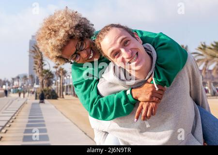 Porträt eines glücklichen jungen Paares, das lachend und Spaß mit der Frau hat, die von ihrem Freund gehuckelt wird, Konzept von Freundschaft und Spaß in einer Beziehung Stockfoto