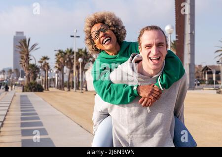 Glückliches junges Paar lachen und Spaß haben mit dem Mann Huckepack ihre Freundin, Konzept der Freundschaft und Spaß in einer Beziehung, kopieren Raum für t Stockfoto
