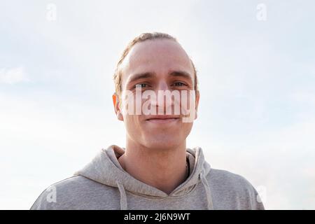 Porträt eines jungen kaukasischen Mannes, glücklich lächelnd und mit Blick auf die Kamera, Himmel im Hintergrund, Konzept von Glück und Lebensstil, Copy Space for Text Stockfoto