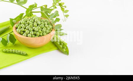 Frische grüne Erbsen in einer Holzschüssel mit Erbsen Pflanzen Blätter auf einer grünen Serviette auf weißem Hintergrund, gesundes Bohnenprotein Stockfoto