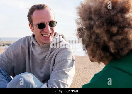 Junger kaukasischer Mann, der lächelt und mit einem nicht erkennbaren Freund spricht, Konzept von Freundschaft und Kommunikation in einer Beziehung Stockfoto